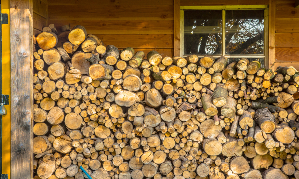 Split firewood logs stacked in a covered log store against a timber cabin wall, seasoning for winter